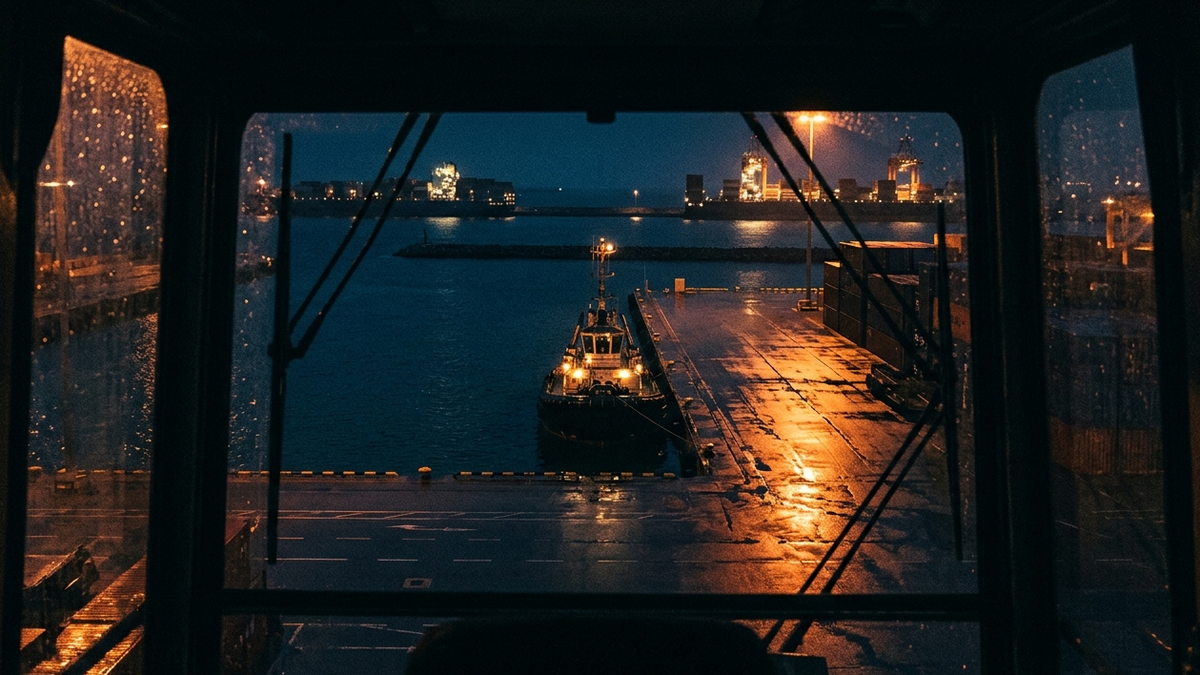 A small tug occupying a berth at night while two large ships wait outside the breakwater